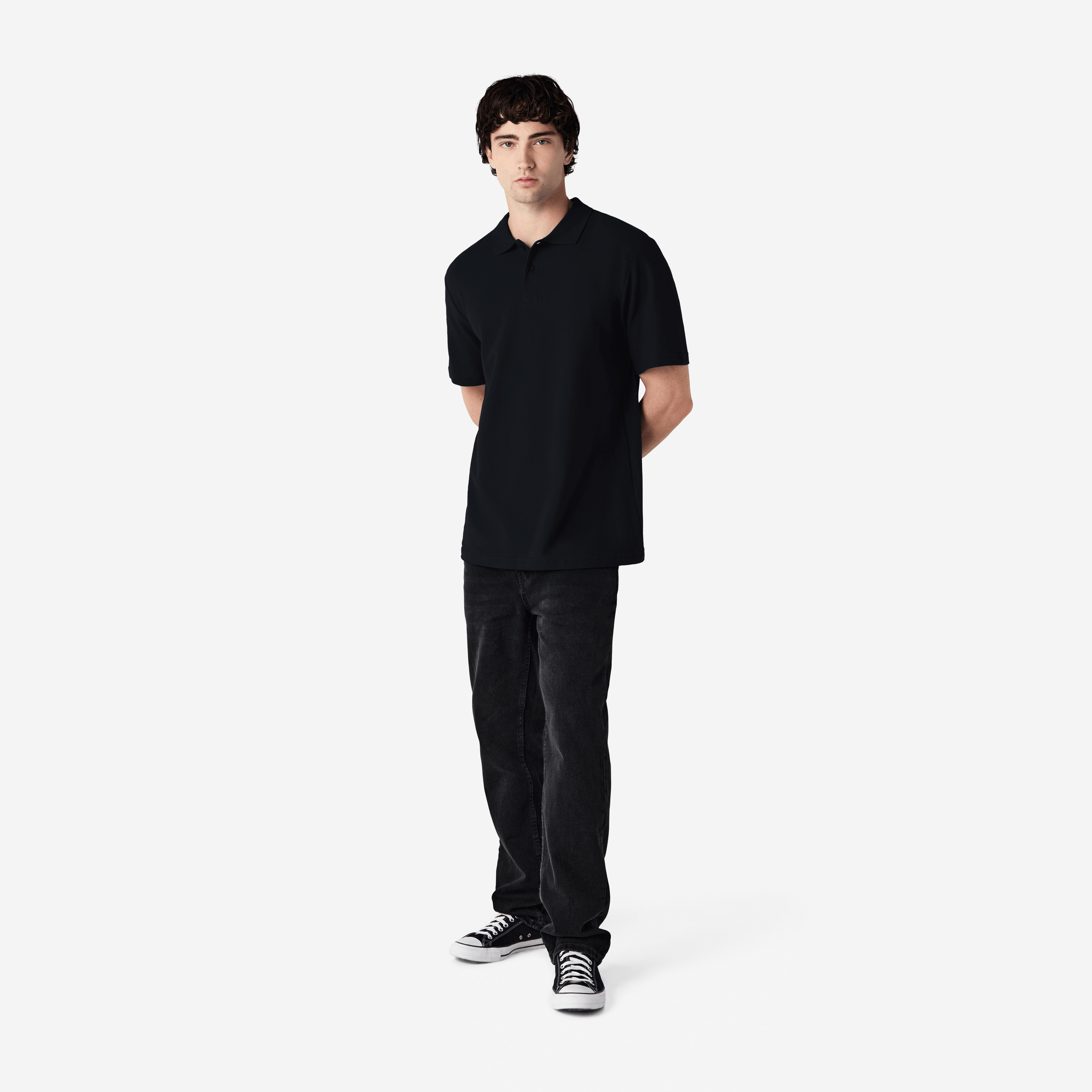 Person wearing a black polo shirt and pants with black and white sneakers on a white background